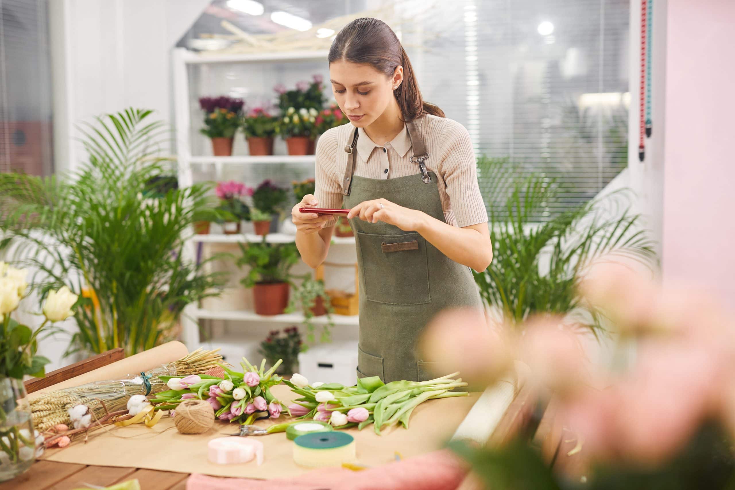 Brunette woman taking behind the scenes pictures and videos for flower shop social media